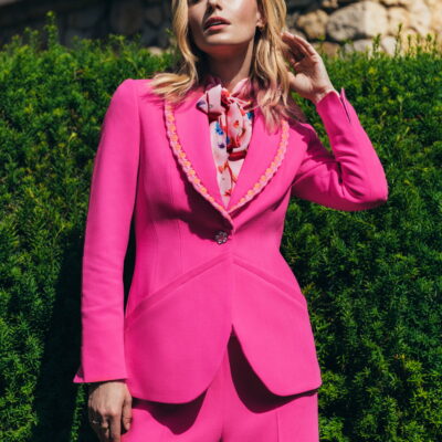 "Frau trägt pinken Blazer mit Häkelkante und Schalkragen von Maison de l’île – Close-up vor grüner Hecke"